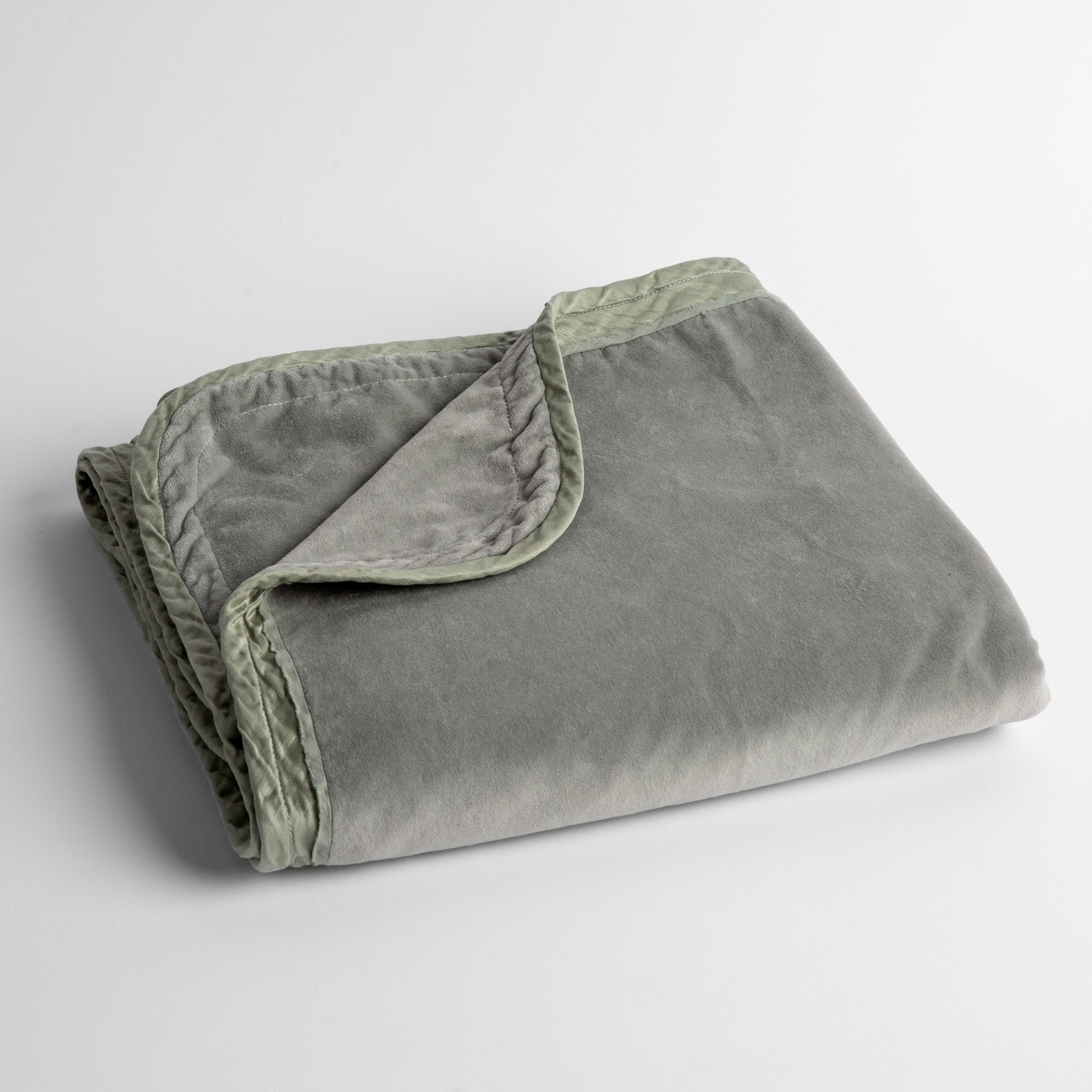 Mineral: cotton velvet baby blanket trimmed with charmeuse, folded with a covern folded back to show trim contrast; shot overhead and at a slight angle against a white background. 