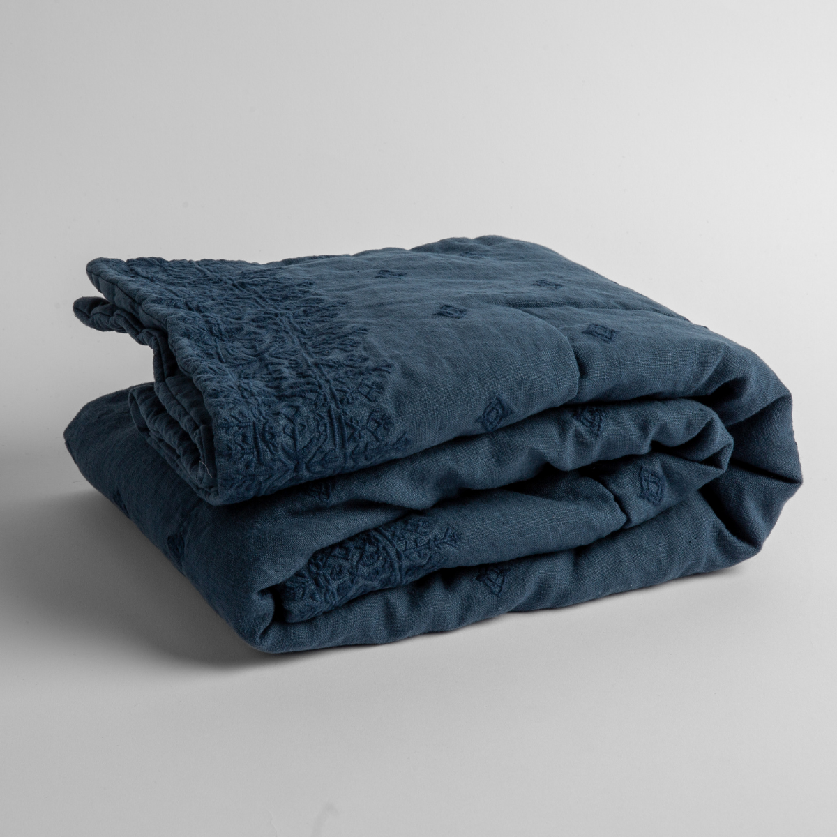 Midnight:  embroidered linen baby blanket folded and shown  overhead from a slight angle against a white background. 