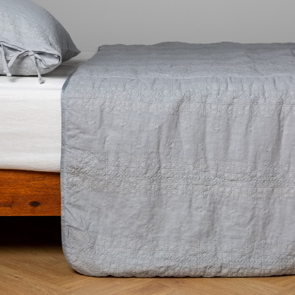 Cloud:  embroidered midweight linen bedspread with matching sham on a bed with a white fitted sheet. Shot from the side view, the bedframe is slightly visible  against a white background and medium wood floor. 