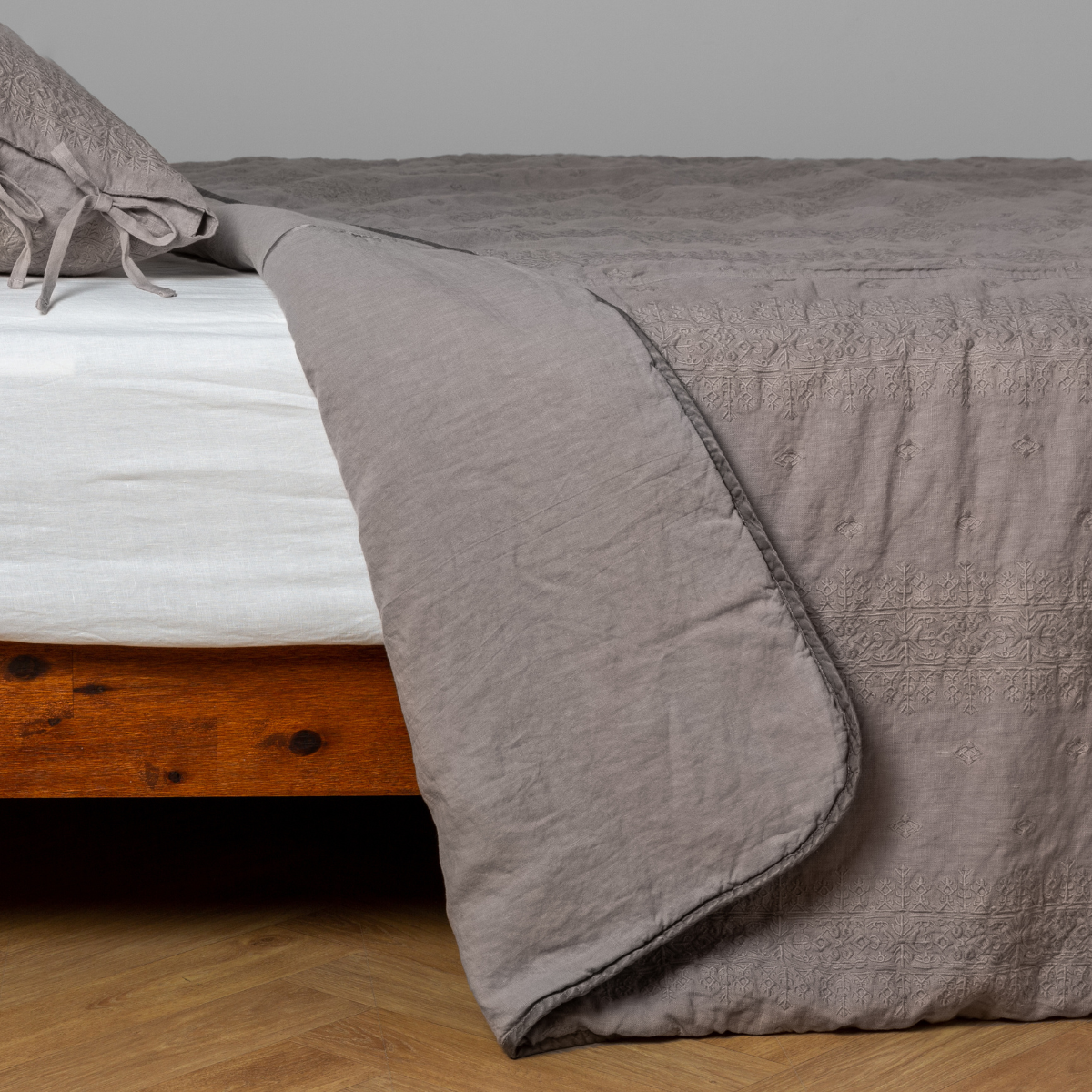 Fog:  White: embroidered bedspread with corner pulled back  showing the plain linen back. Shown with a white fitted sheet and matching sham, the bedframe is slightly visible  and the bed is against a white wall and on a medium wood floor. 