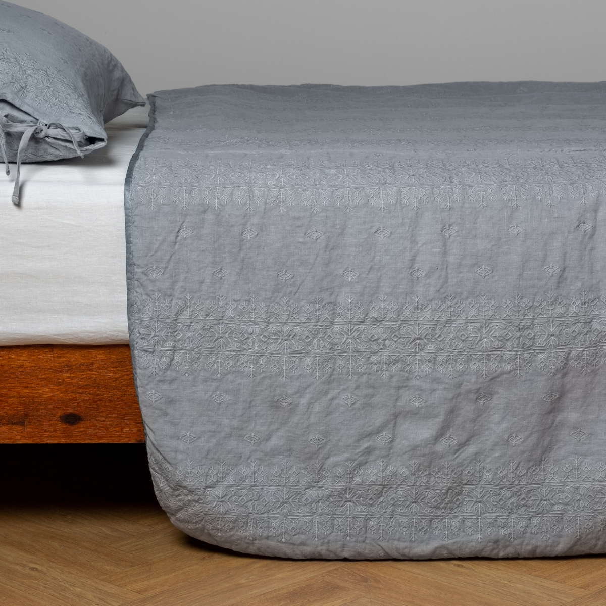 Mineral: embroidered midweight linen bedspread with matching sham on a bed with a white fitted sheet. Shot from the side view, the bedframe is slightly visible  against a white background and medium wood floor. 