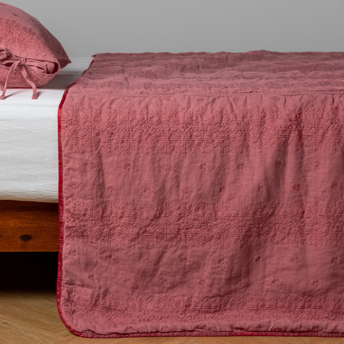Poppy: embroidered midweight linen bedspread with matching sham on a bed with a white fitted sheet. Shot from the side view, the bedframe is slightly visible  against a white background and medium wood floor. 