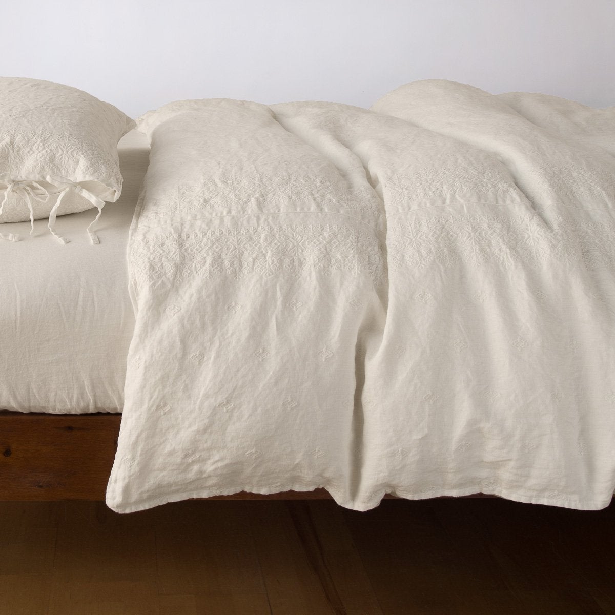 Parchment: lightly rumpled duvet cover on a monochromatic bed against a white background - side view.