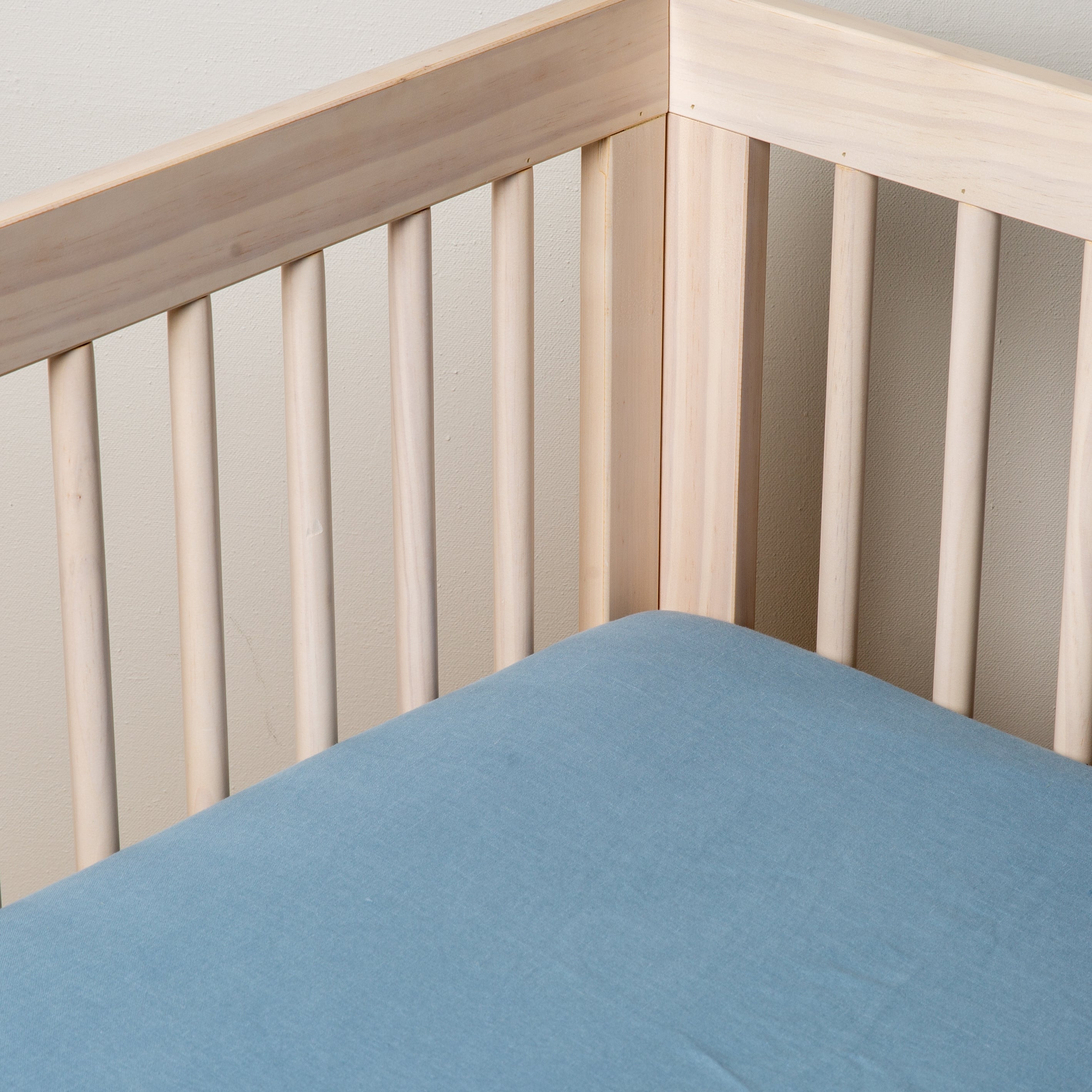 Tahoe Blue: linen crib sheet on the mattress shot slightly overhead into the corner of a white crib. against a white background. 