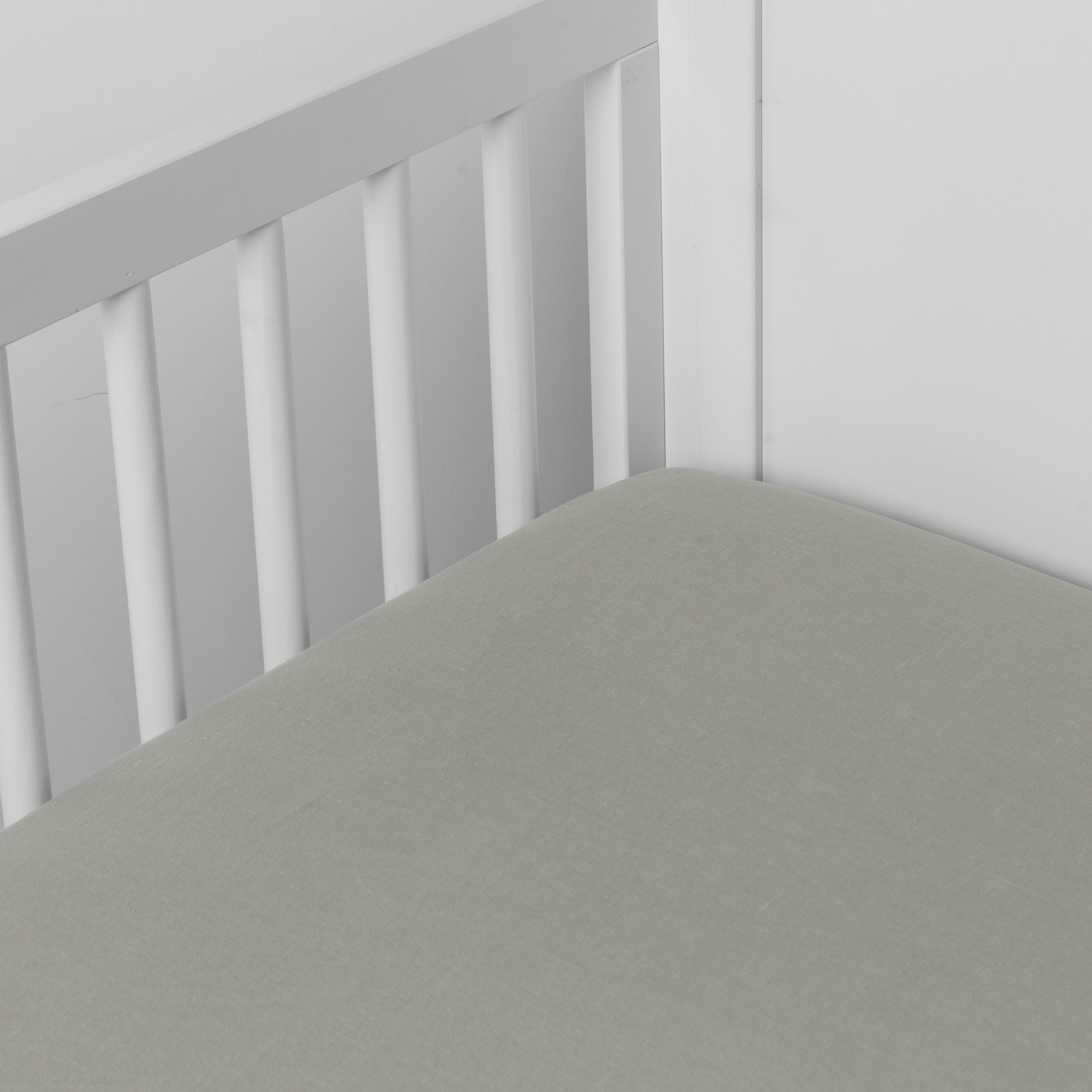 Eucalyptus: linen crib sheet on the mattress shot slightly overhead into the corner of a white crib. against a white background. 