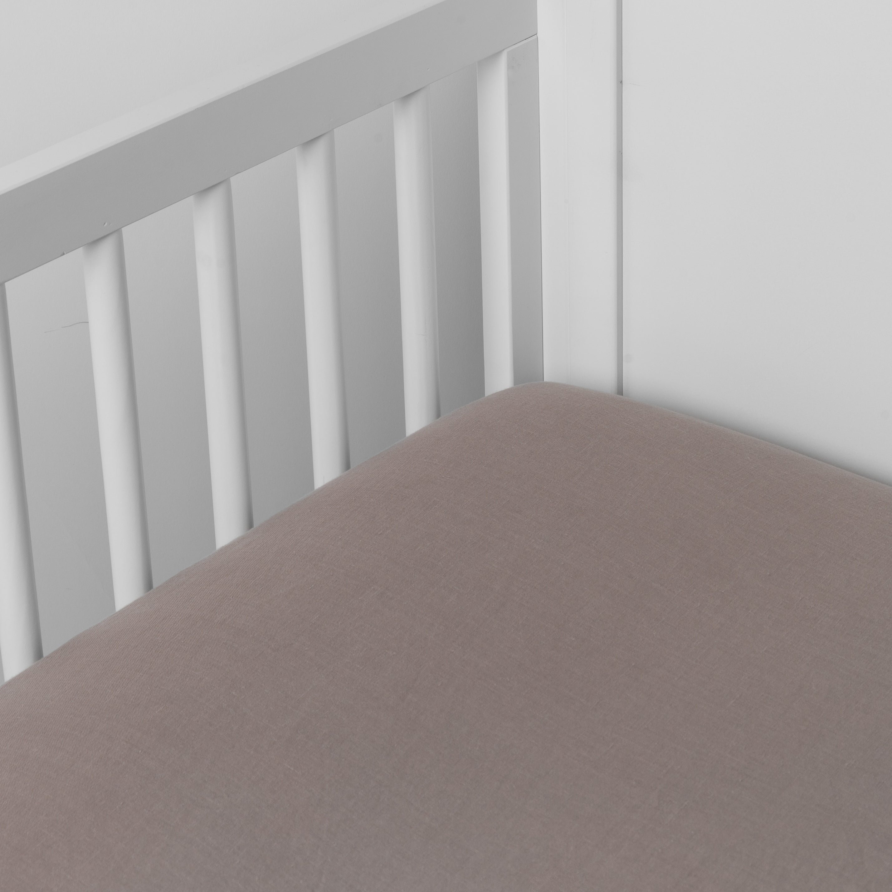 Moonlight: linen crib sheet on the mattress shot slightly overhead into the corner of a white crib. against a white background. 