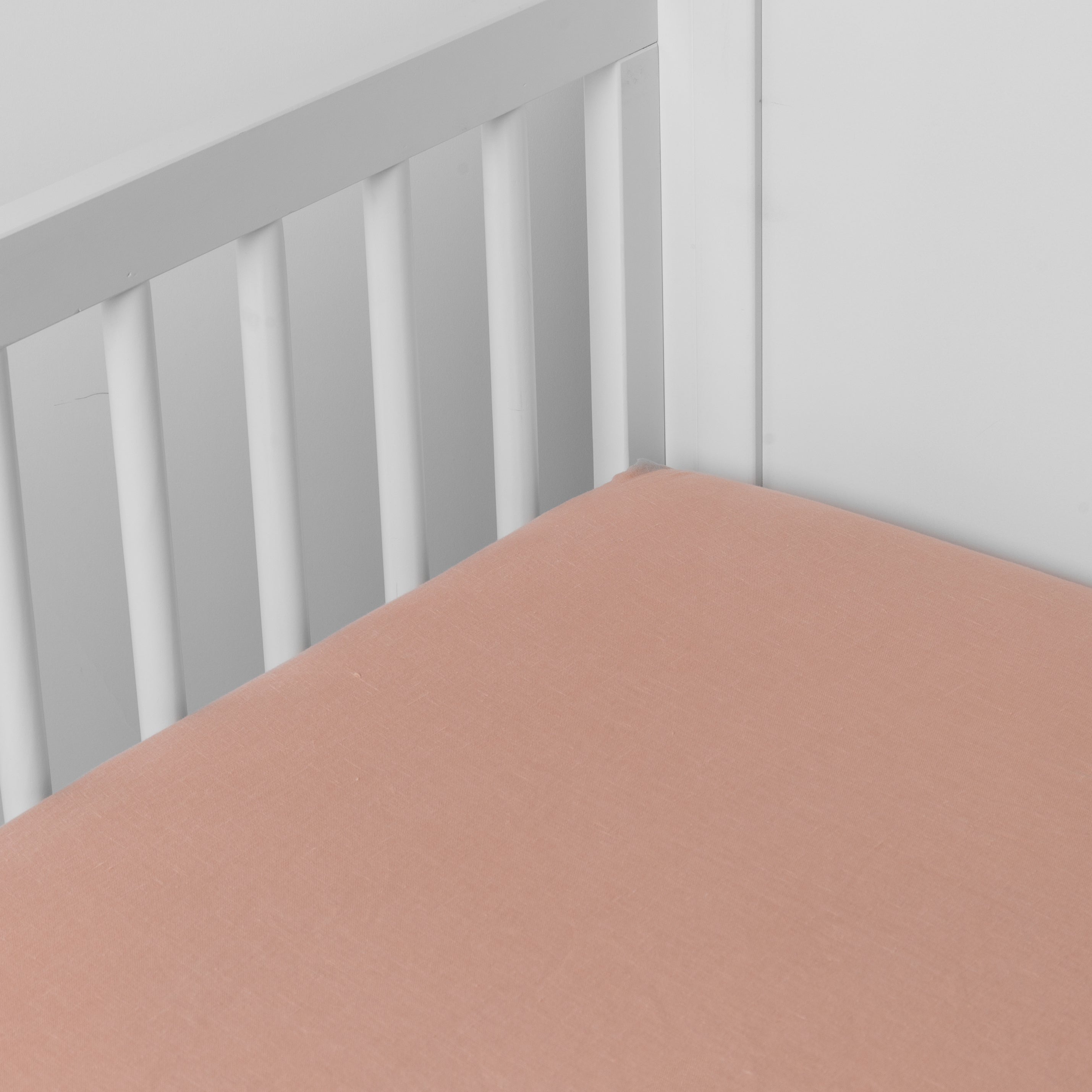 Rouge:  linen crib sheet on the mattress shot slightly overhead into the corner of a white crib. against a white background. 