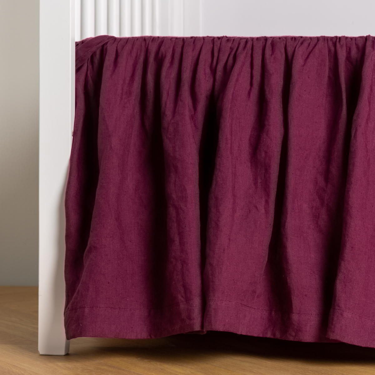 Fig:  crib skirt shown on a white crib with no mattress against a white wall and medium wood flooring. 