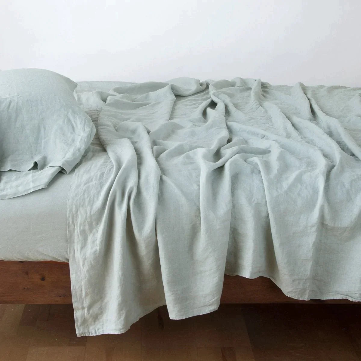 [allvariants]: Rumpled linen flat sheet in eucalyptus, with matching fitted sheet and sleeping pillow - side view.