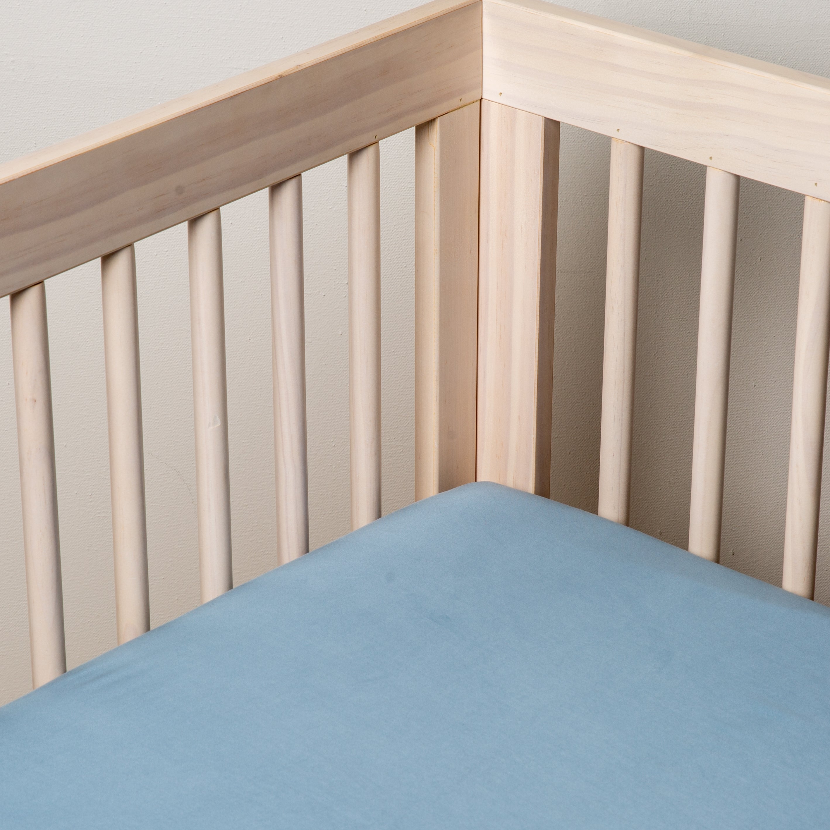 Tahoe Blue: a blue tencel crib sheet shown into the corner of a natural wood crib. 