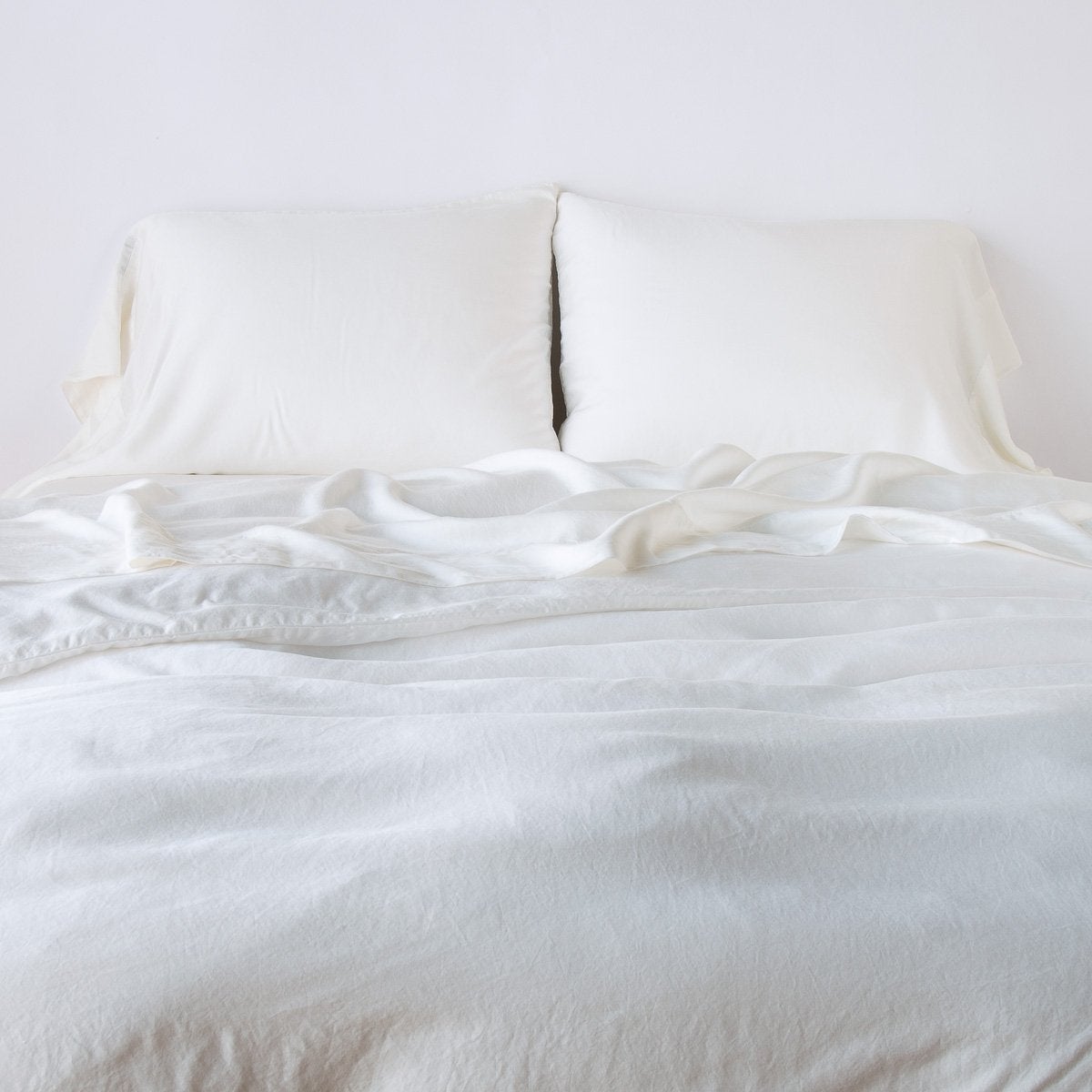 : Madera Luxe duvet cover in winter white with monochromatic sheeting and sleeping pillows, agaisnt a plain white background - close-up end of bed view.