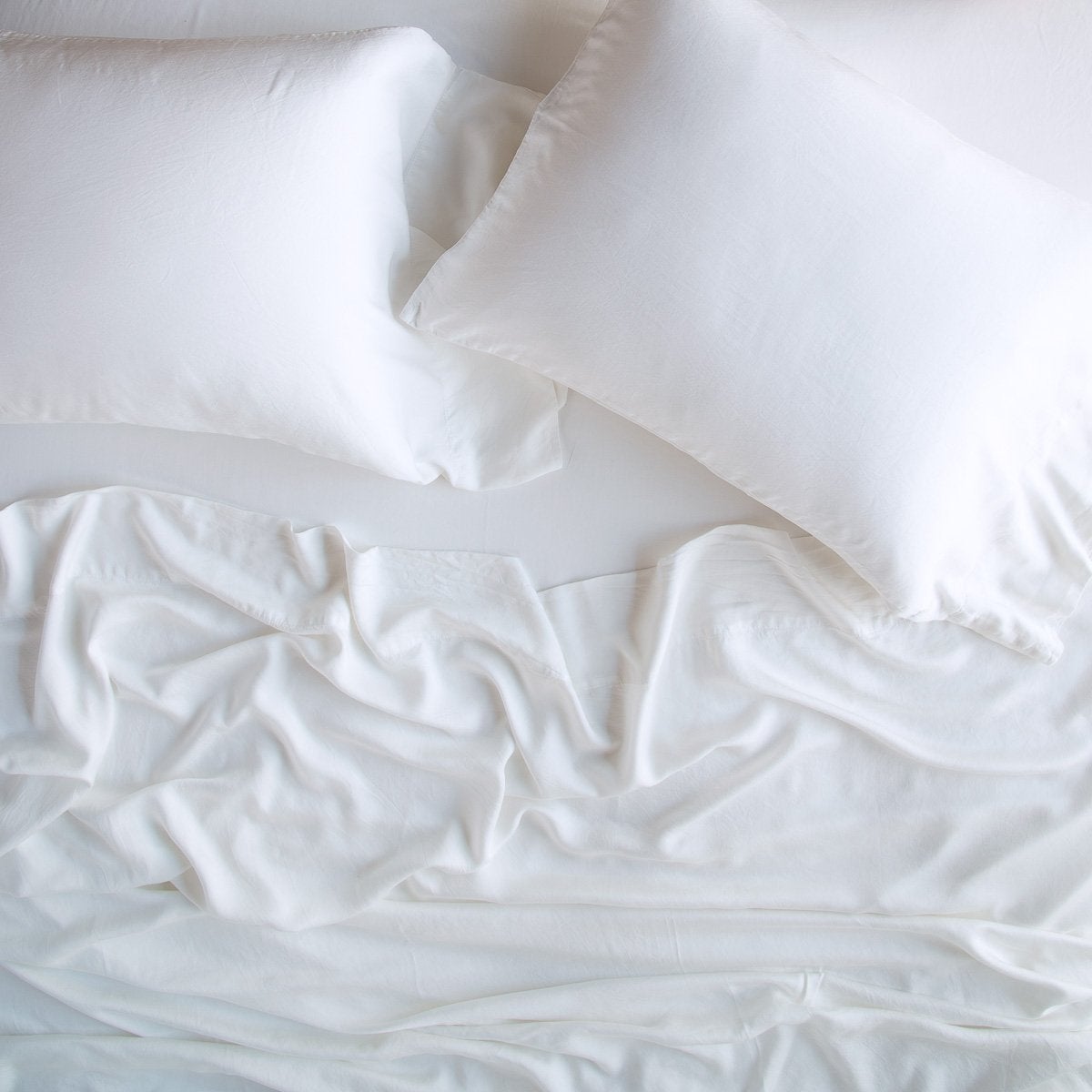 White: sleeping pillows laid flat over rumpled matching sheeting - overhead view.