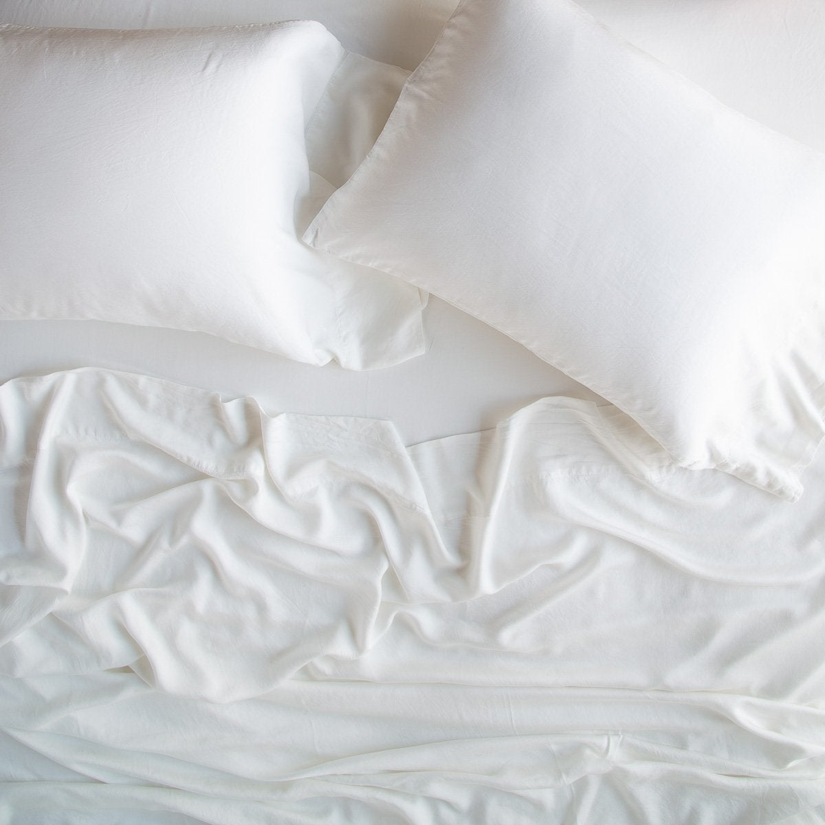 : Madera Luxe sleeping pillows laid flat over rumpled matching sheeting - winter white, overhead view.