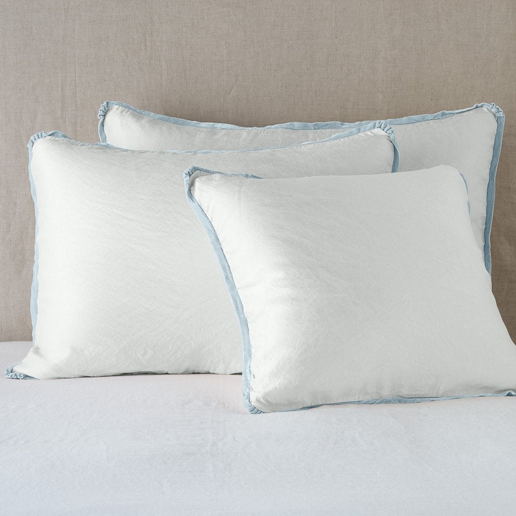 Cloud: shams leaning upright on white sheeting against a neutral headboard.