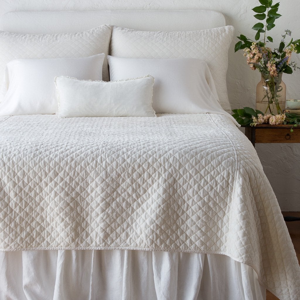 : Silk velvet quilted shams with matching coverlet on a neatly-made, monochromatic bed - winter white, end of bed view.