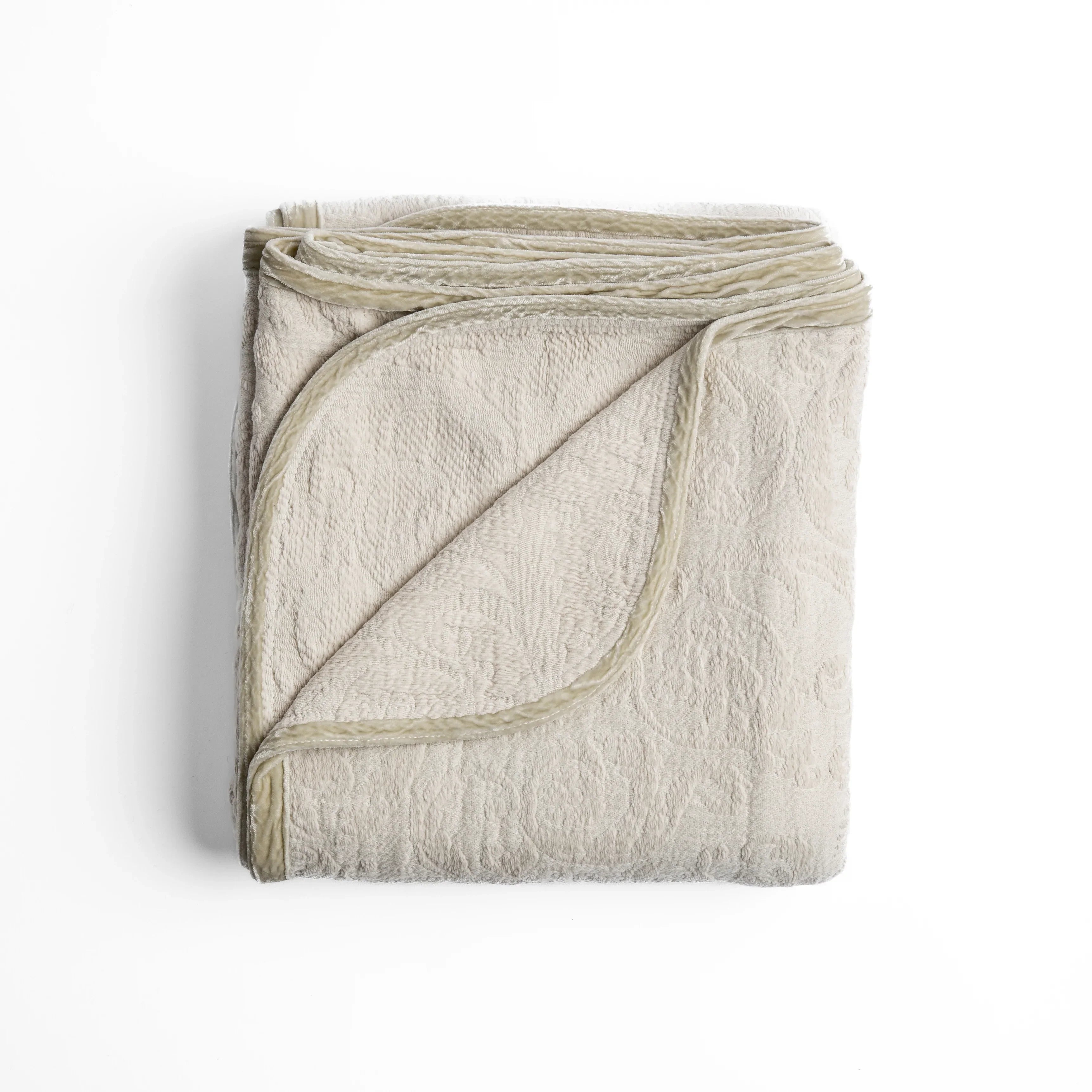 Parchment: folded organic cotton damask throw blanket shown with the corner folded down to show silk velvet trim detail — overhead against a plain white background. 