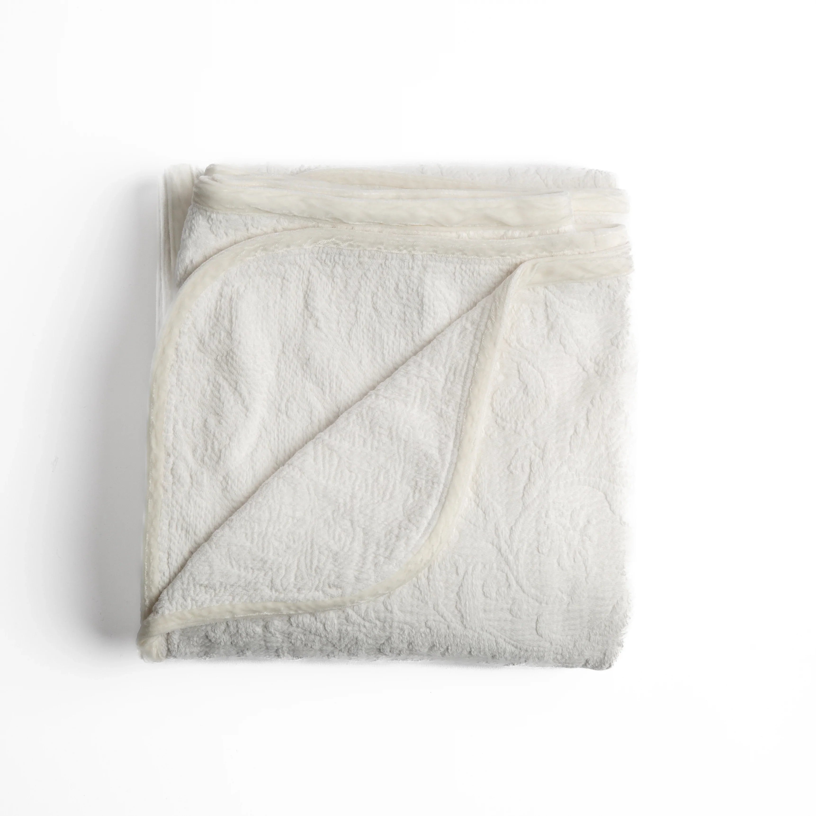 Winter White: folded organic cotton damask throw blanket shown with the corner folded down to show silk velvet trim detail — overhead against a plain white background. 