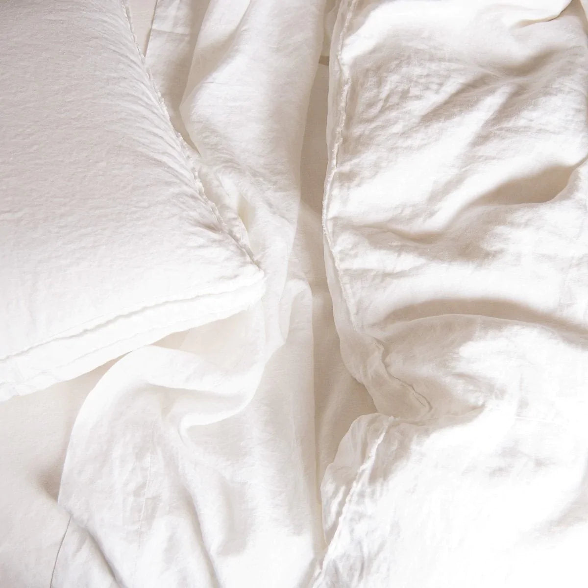 : Austin duvet cover with linen sheets and pillows in monochromatic white. Overhead close up angle highlights the raw-edge trim detail.