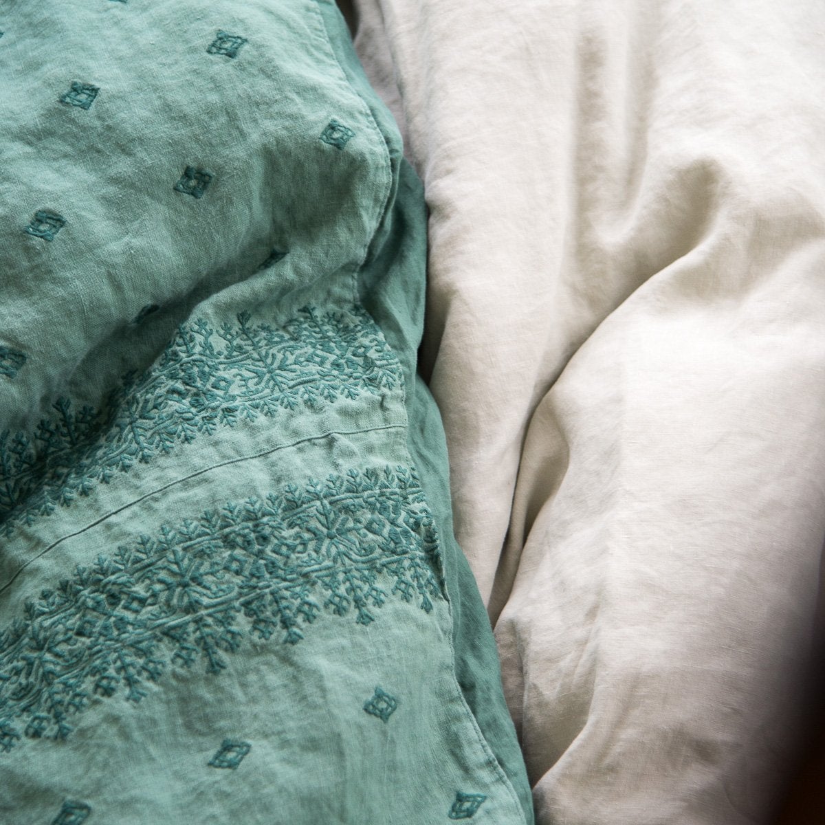 : Close-up of Ines duvet cover in jade against light linen sheets, showcasing the embroidery pattern detail - overhead view.