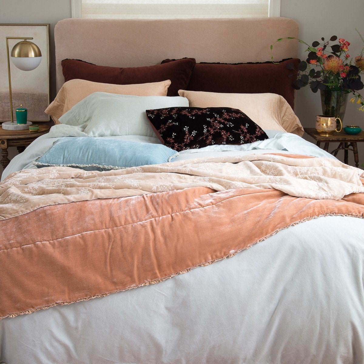 : Lynette throw blanket in pearl, layered with pink, brown and blue tones in cotton velvet and silk velvet on a rumpled bed - end of bed view.