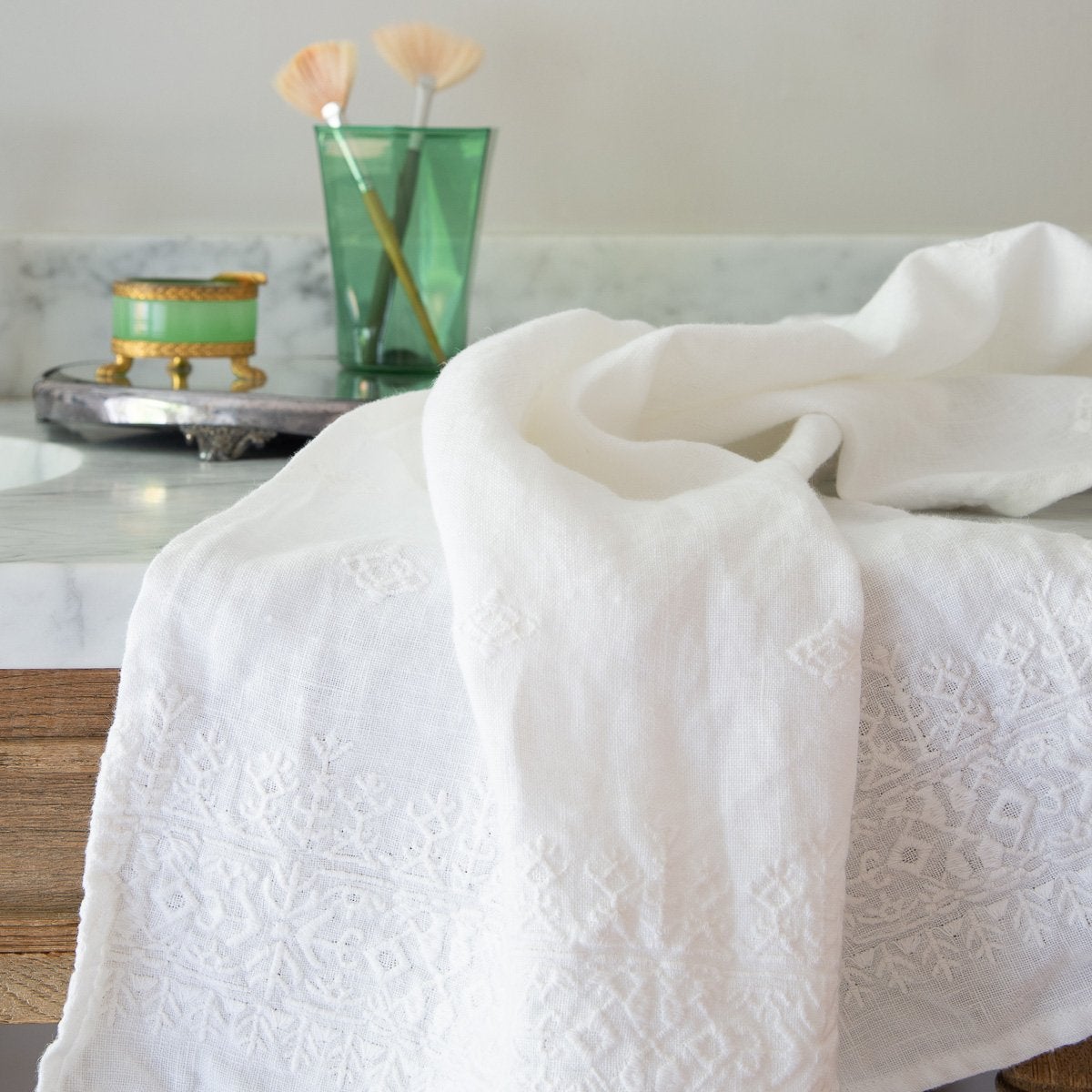 [allvariants]: White Ines guest towel draped over a marble bathroom counter with green glass accessories in the background.