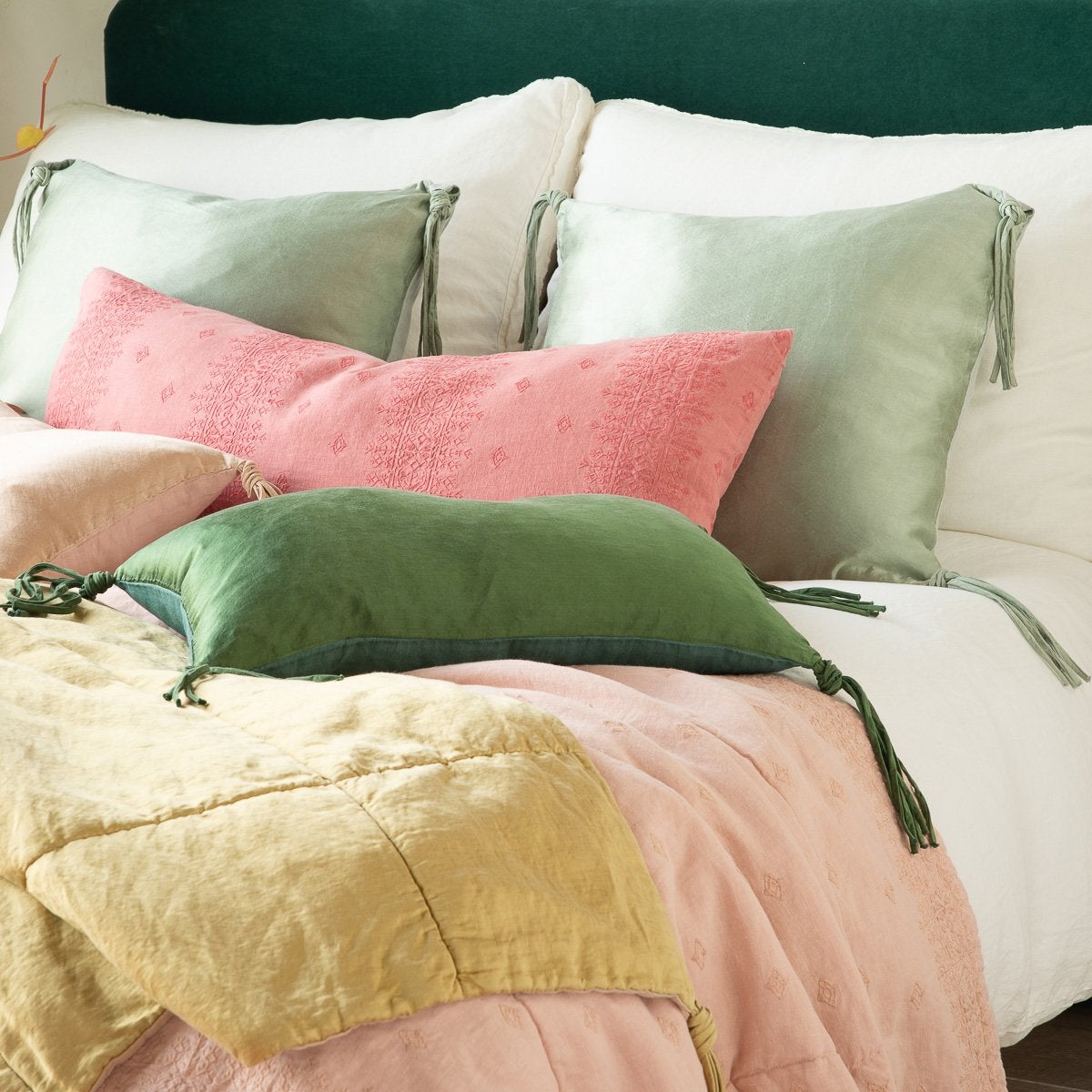 : Ines throw blanket in rouge, layered under green, pink, and gold tones on a white bed, - cropped three-quarter angle.