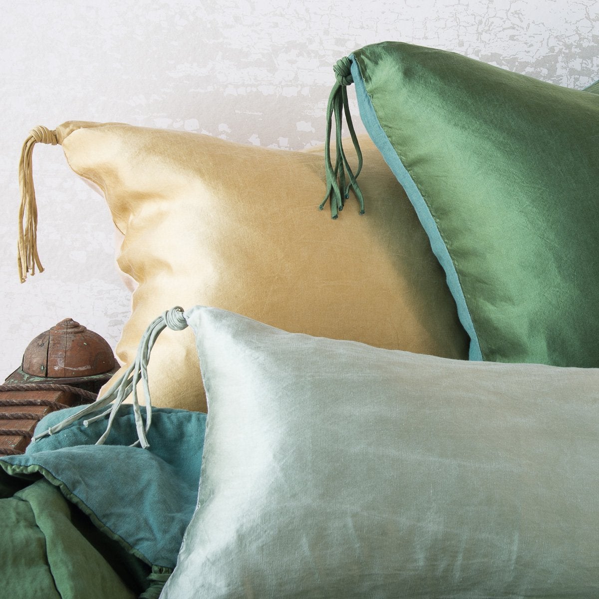 : Close-up of three Taline throw pillows in green and gold tones, showcasing the corner tassel details.