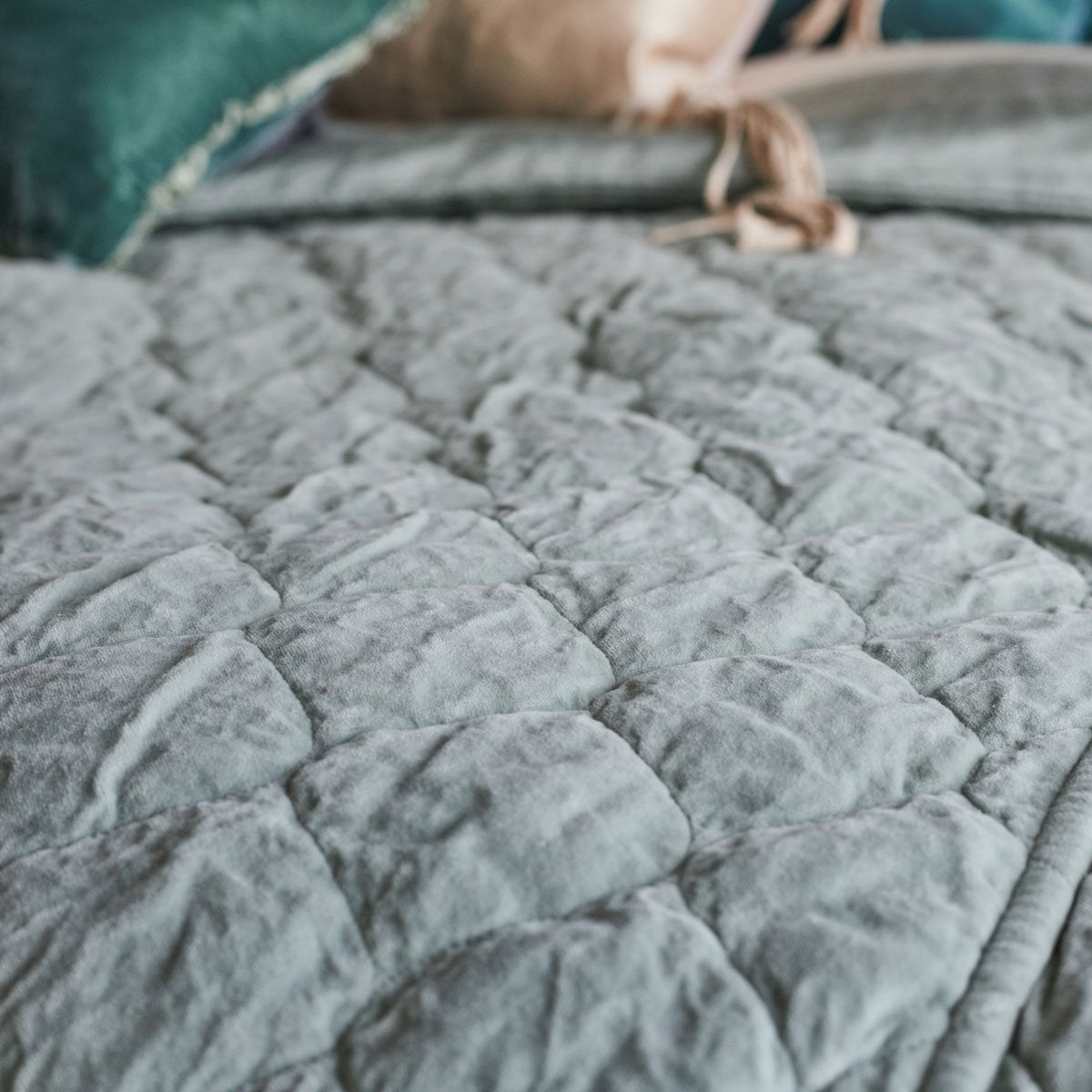 : Close-up of Harlow quilted coverlet in mineral, with pops of green and pink throw pillows in the top of the frame - overhead angle.