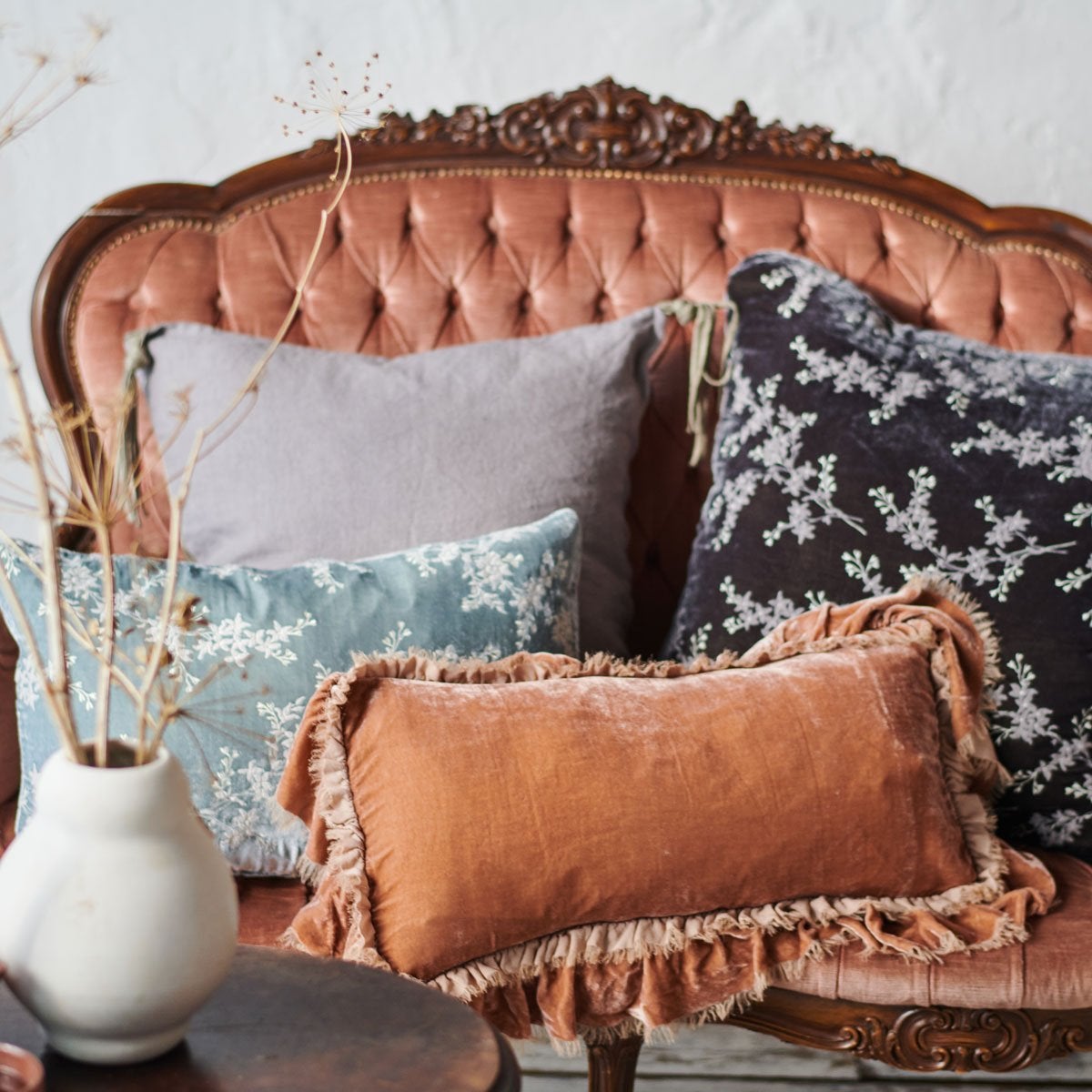 : Loulah Accent pillow in rouge, layered against grey and blue tones on a vintage loveseat.