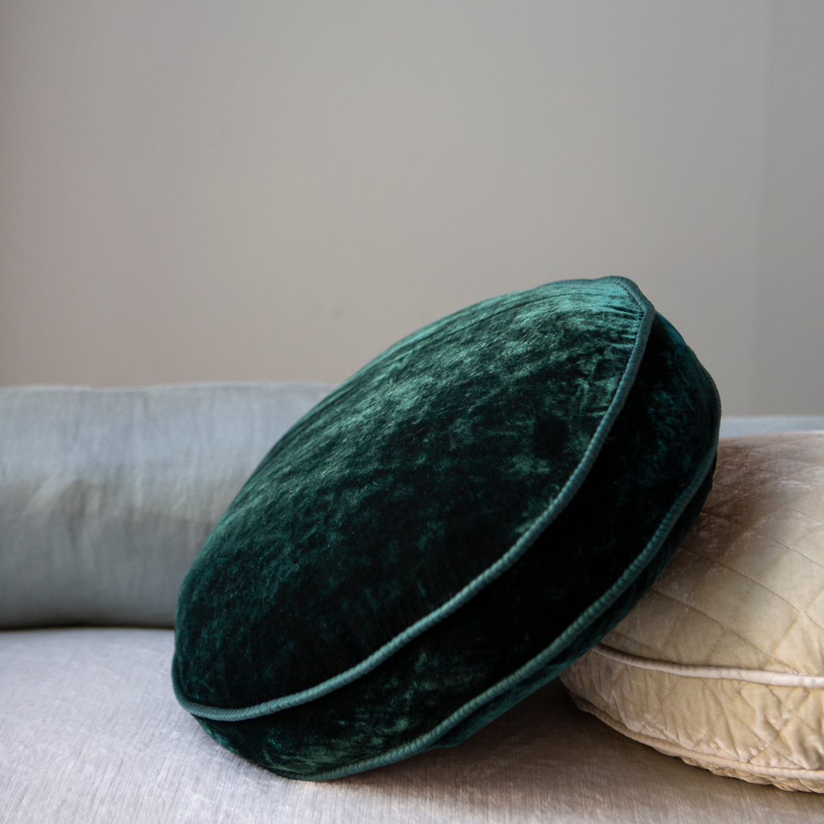 : Jade silk velvet round pillow with satin trim centered with other throw pillows. 