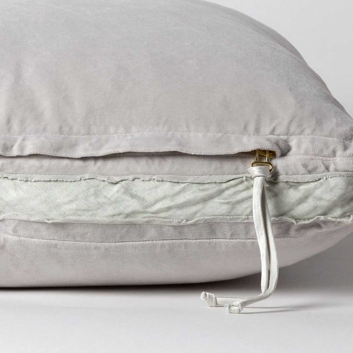 Sterling: Close-up of charmeuse gusset, raw-edge trim, and brass zipper detail on Harlow pillow - side view.