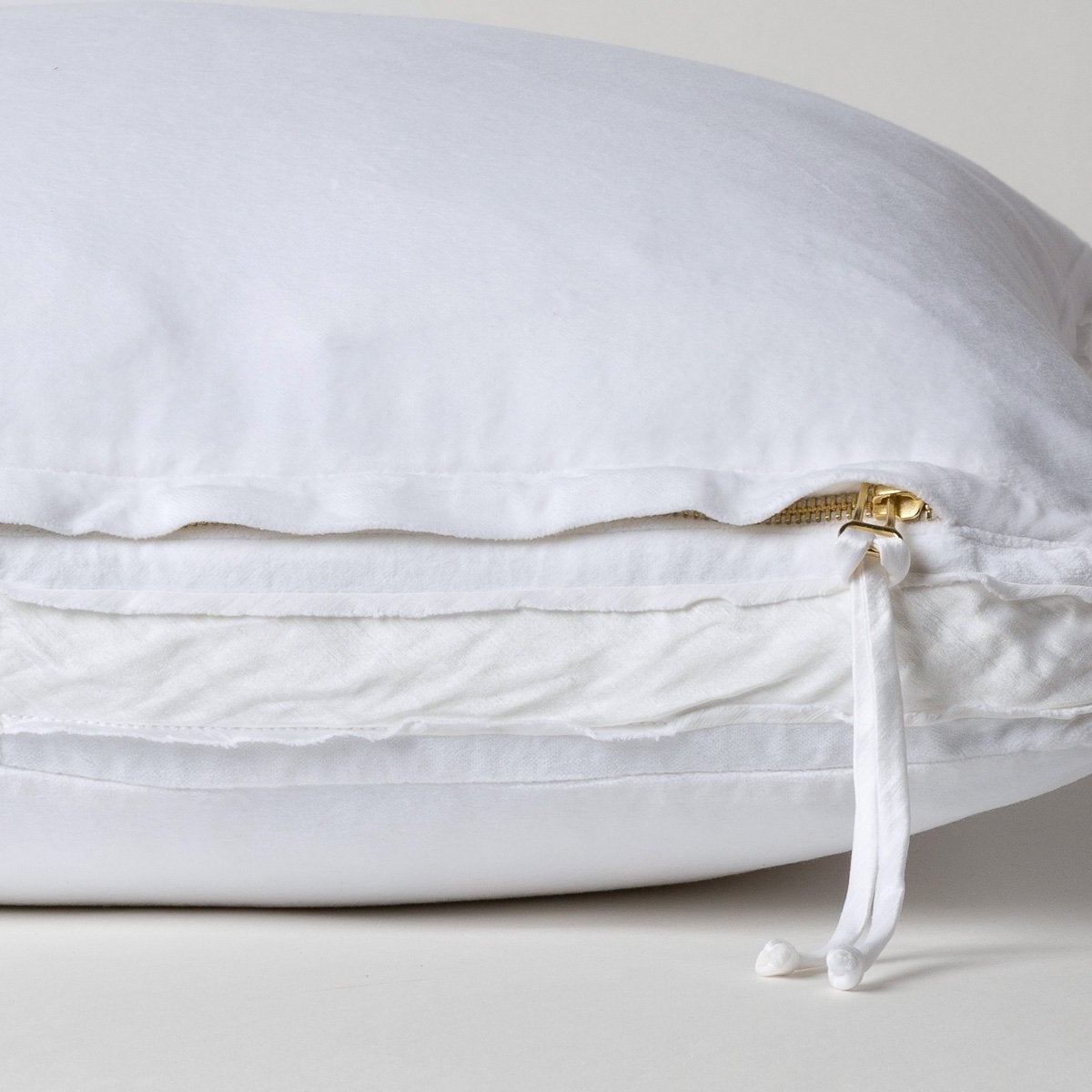 White: Close-up of charmeuse gusset, raw-edge trim, and brass zipper detail on Harlow pillow - side view.