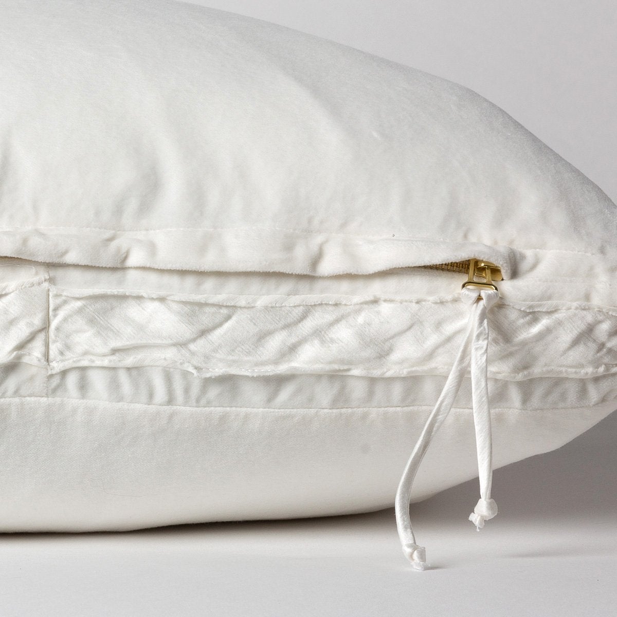 Winter White: Close-up of charmeuse gusset, raw-edge trim, and brass zipper detail on Harlow pillow - side view.