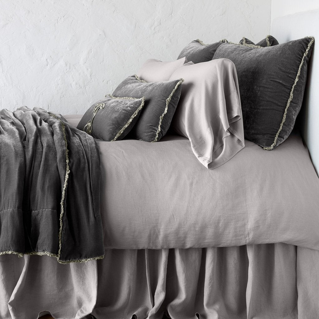 Fog: Silk velvet lumbar pillow with petite ruffle on a monochromatic, neatly made bed with matching accessory pieces - side view.