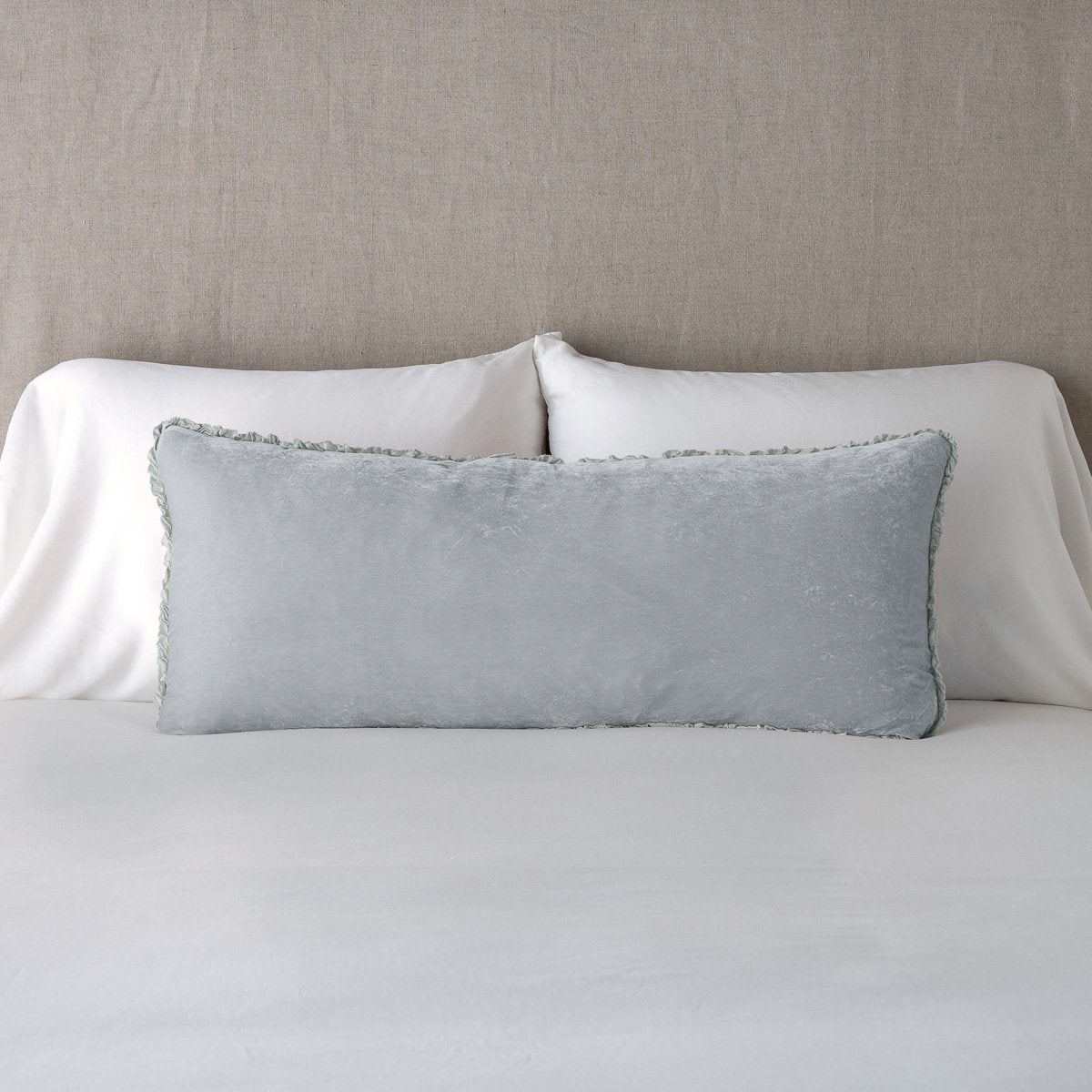 Sterling: Silk velvet lumbar pillow with petite ruffle, leaning upright against neutral bedding and headboard.