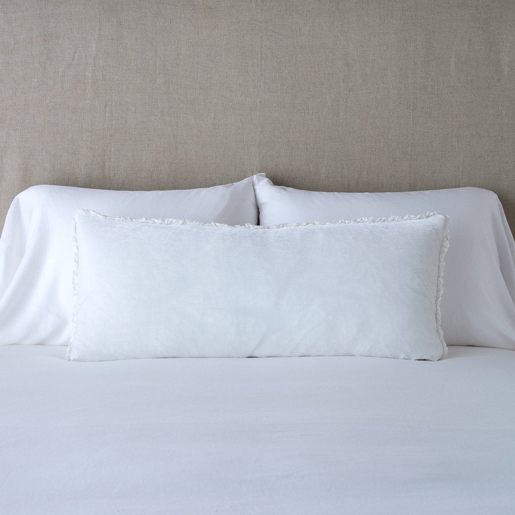 White: Silk velvet lumbar pillow with petite ruffle, leaning upright against neutral bedding and headboard.