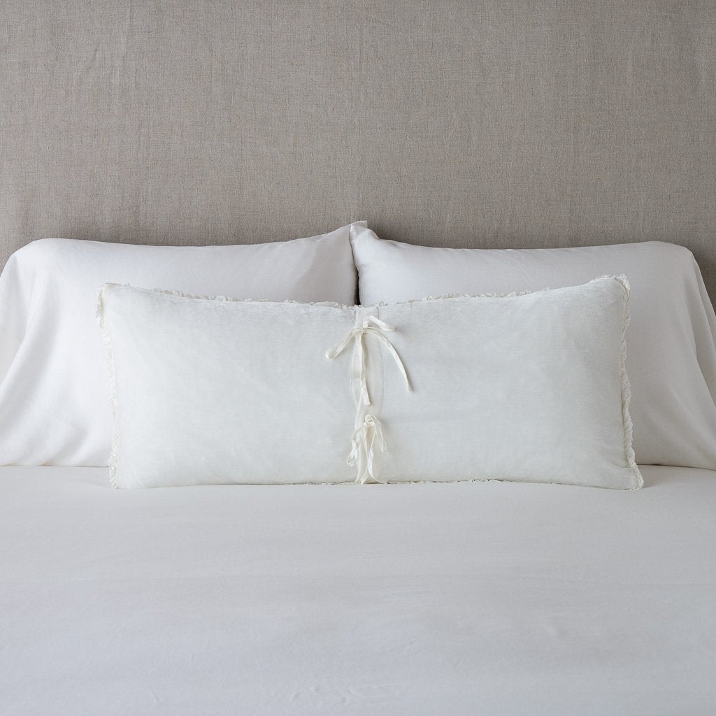 Winter White: Silk velvet lumbar pillow with petite ruffle leaning upright and backwards against neutral bedding and headboard, showcaseing the silk charmeuse tie closures.