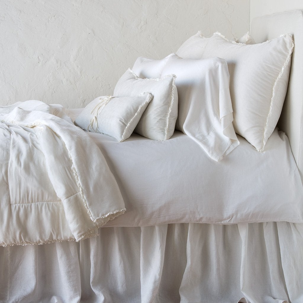 Winter White: Silk velvet lumbar pillow with petite ruffle on a monochromatic, neatly made bed with matching accessory pieces - side view.