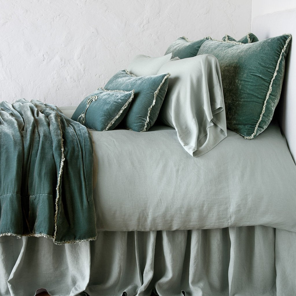 Eucalyptus: Silk velvet throw blanket with petite ruffle, draped across a monochromatic bed - side view.