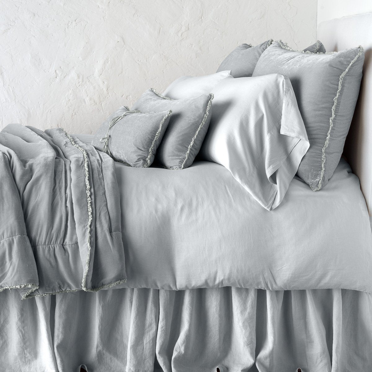 Sterling: Silk velvet throw blanket with petite ruffle, draped across a monochromatic bed - side view.