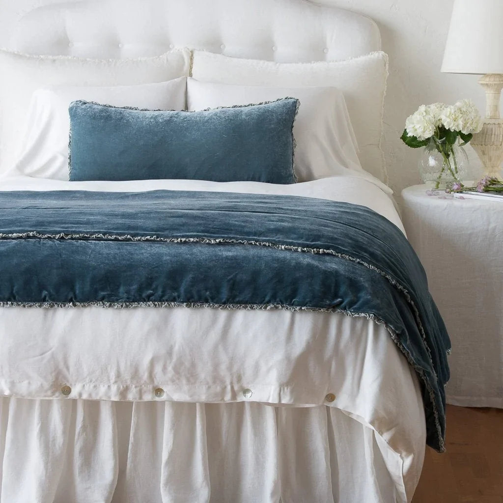 Mineral: Silk velvet shams with a petite ruffle on a white bed, stacked behind sleeping and throw pillows - view from end of bed.