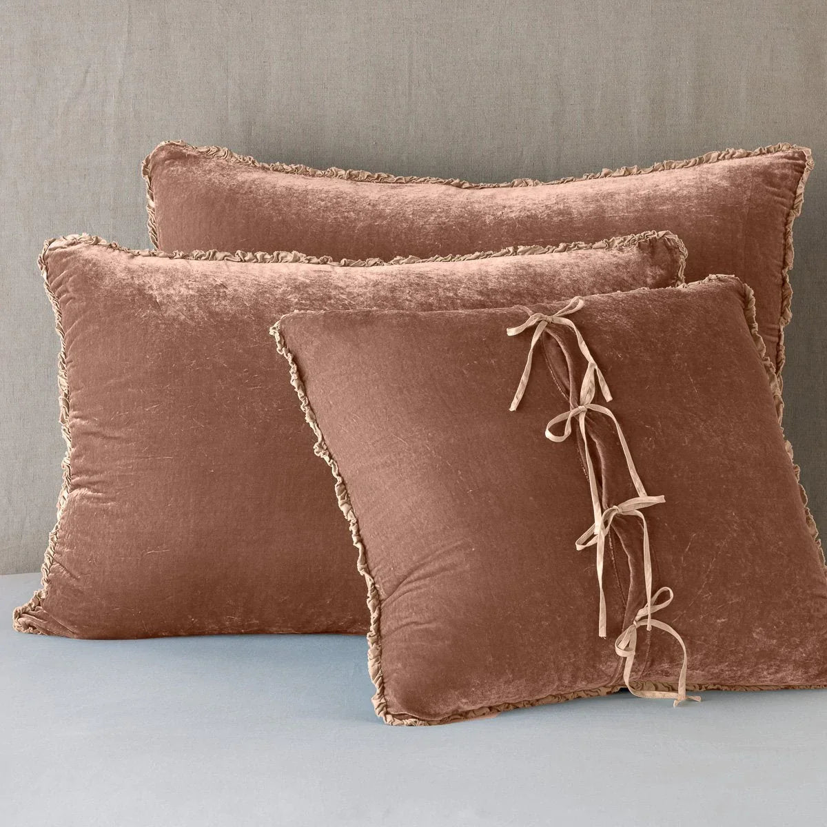 Rouge: Silk velvet  shams with a petite ruffle leaning upright against a neutral headboard. The front sham is backwards, showcasing the charmeuse tie closures.