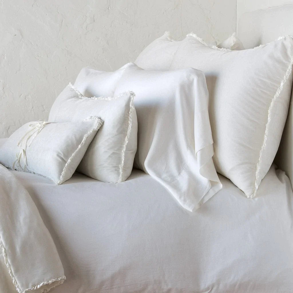 Winter White: Silk velvet shams with a petite ruffle on monochromatic bed, leaning upright behind sleeping and throw pillows - side view.