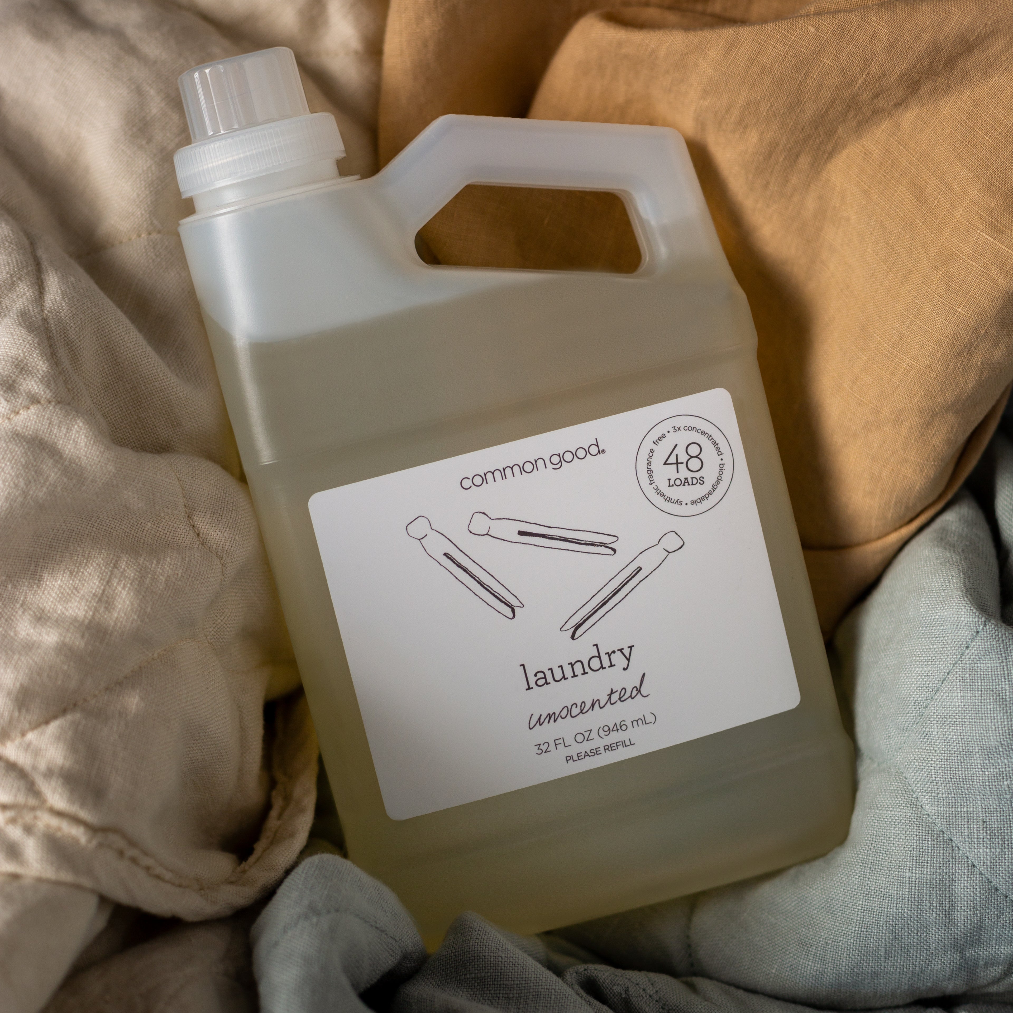 : a bottle of unscented common good laundry detergent shown from overhead  nested in linen fabrics in various colors. 