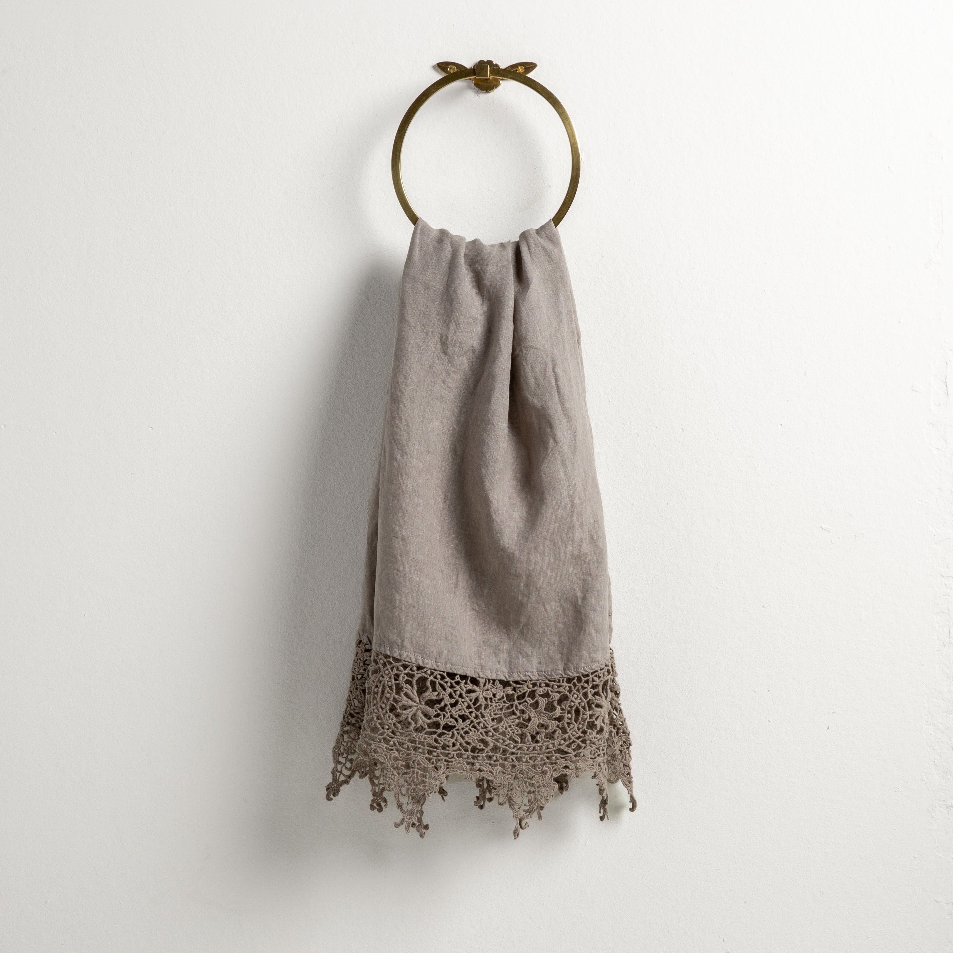 Fog: Lace trimmed linen guest towel  draped through a decorative towel ring against a plain white background.