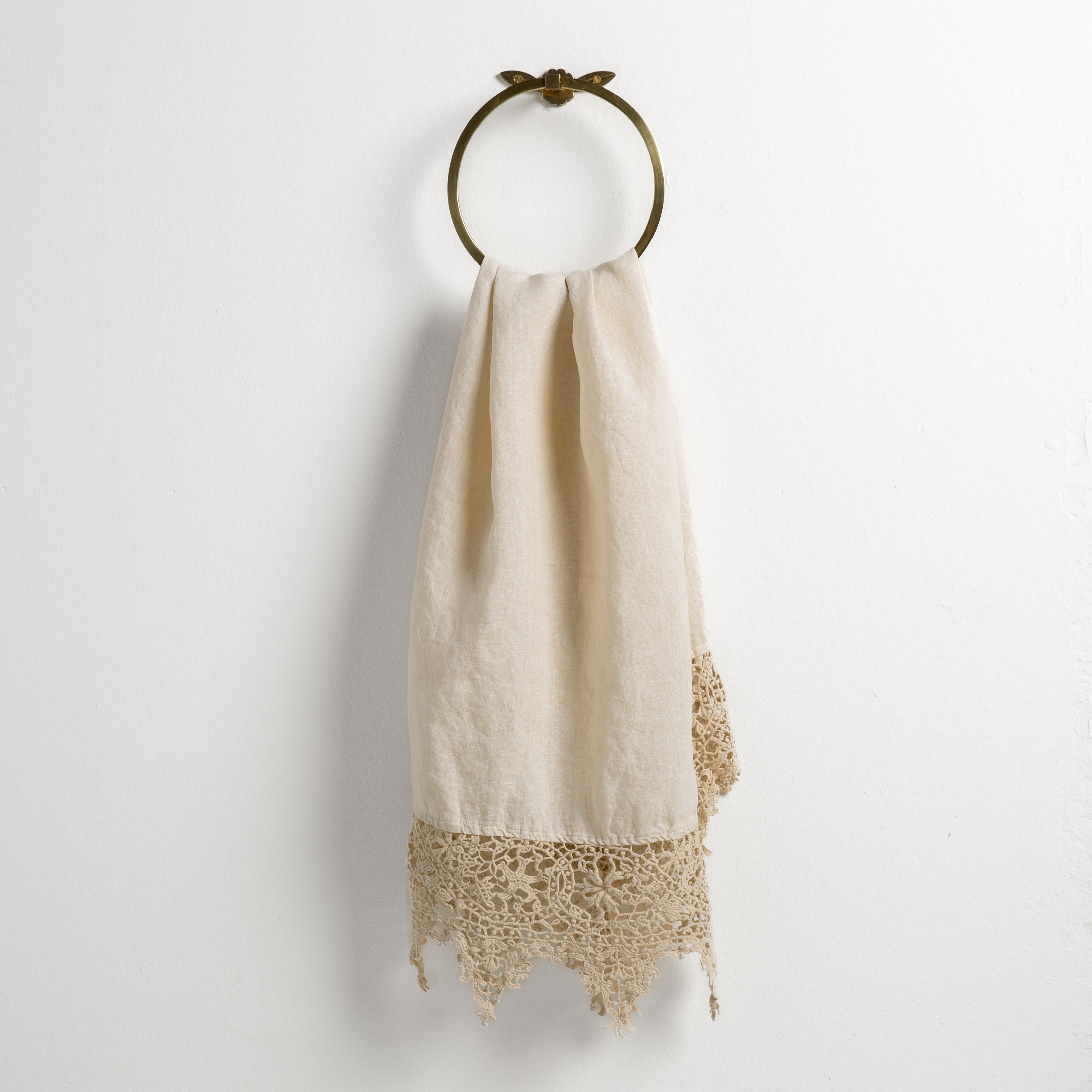 Parchment: Lace trimmed linen guest towel  draped through a decorative towel ring against a plain white background.