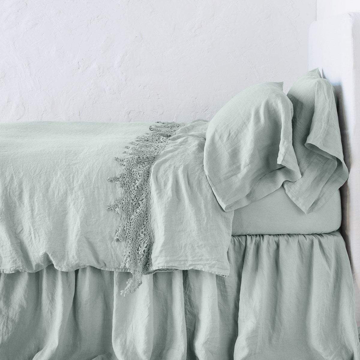Eucalyptus: Lace trimmed linen flat sheet folded back over monochromatic linen bed - side view. 