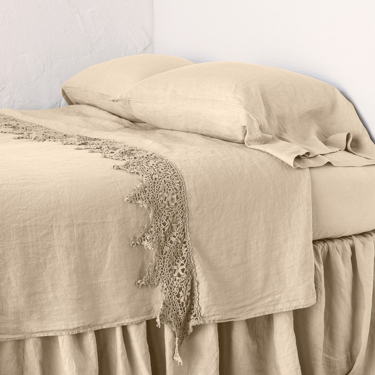 Honeycomb: Lace trimmed linen flat sheet neattly folded back on a monochromatic linen bed - cropped three-quarter angle..
