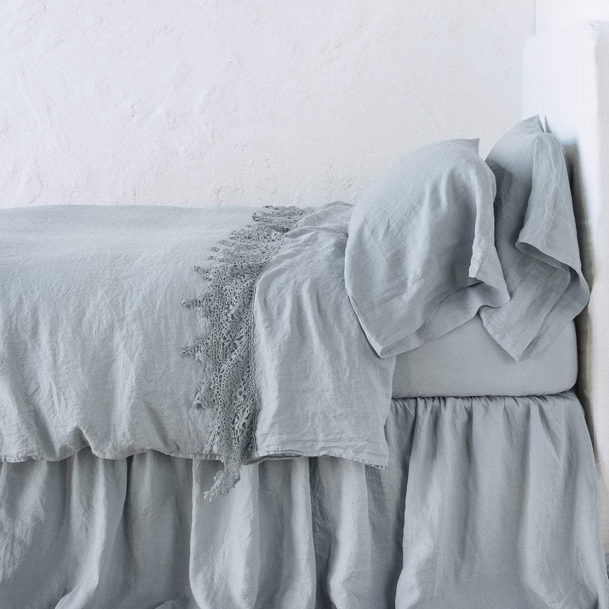 Mineral: Lace trimmed linen flat sheet folded back over monochromatic linen bed - side view. 