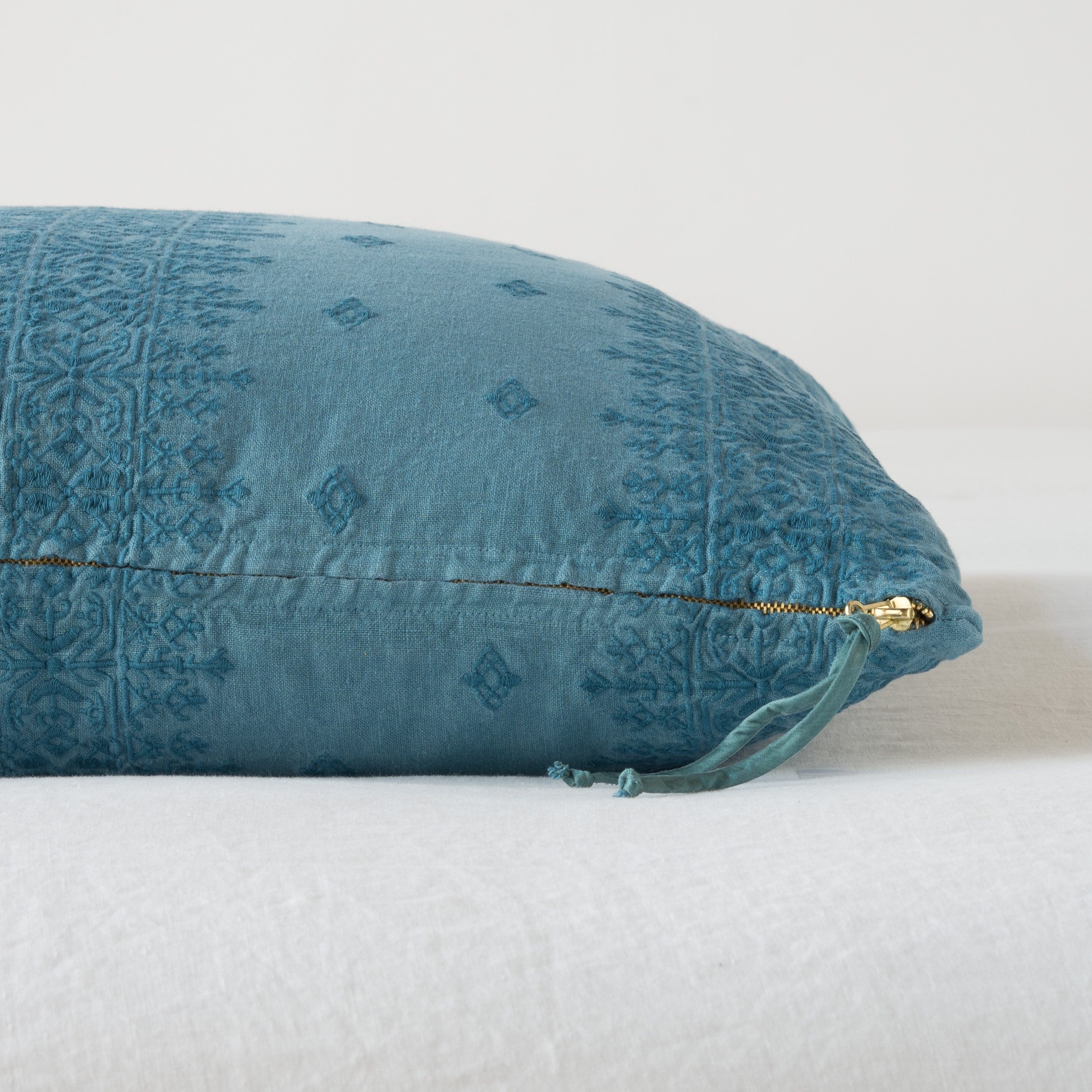 Cenote: Close-up of brass zipper and charmeuse pull details on throw pillow - side view.